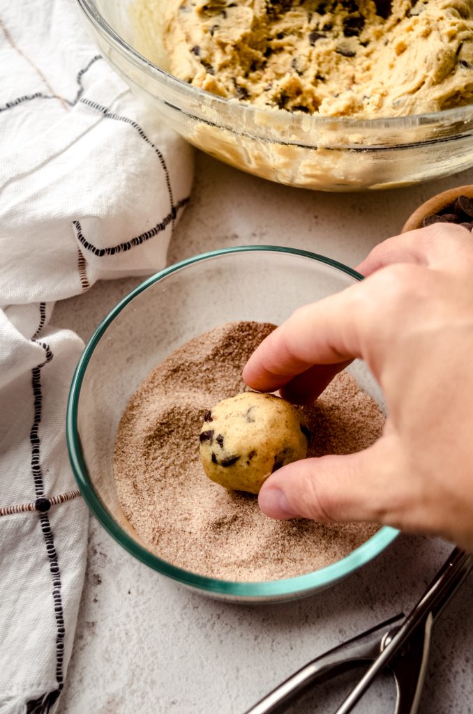 Someone is rolling a ball of chocolate chip snickerdoodle cookie dough into a cinnamon-sugar coating.