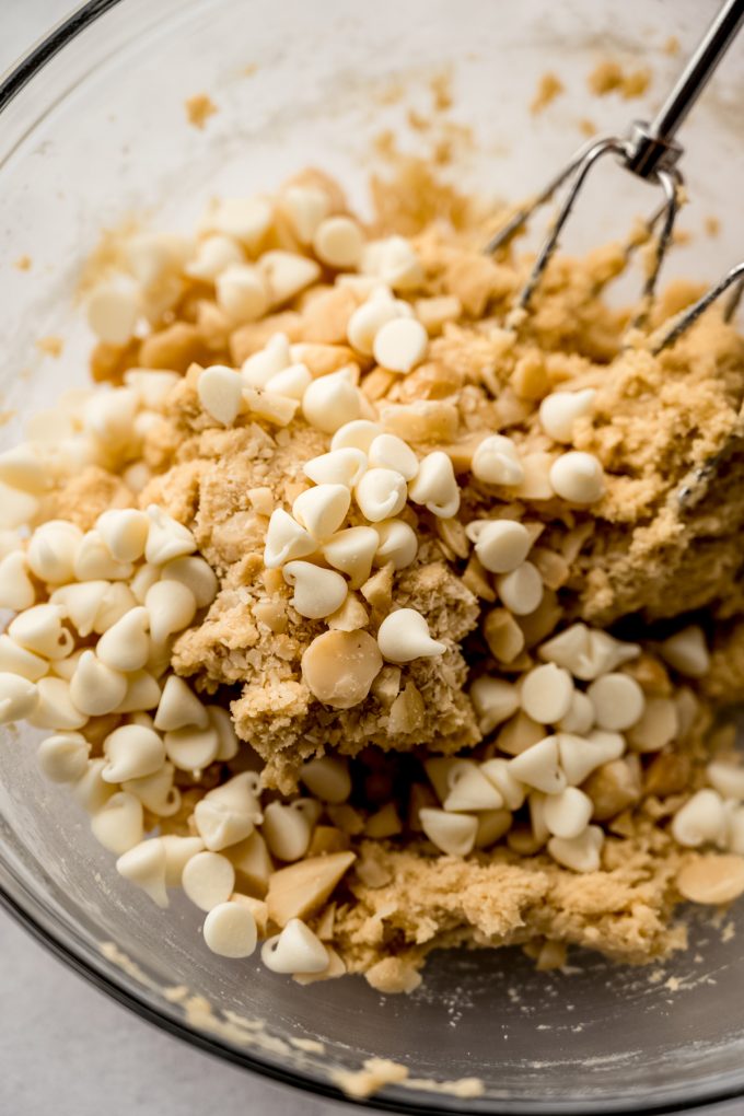 White chocolate macadamia nut cookie dough in a bowl with electric beaters in it.