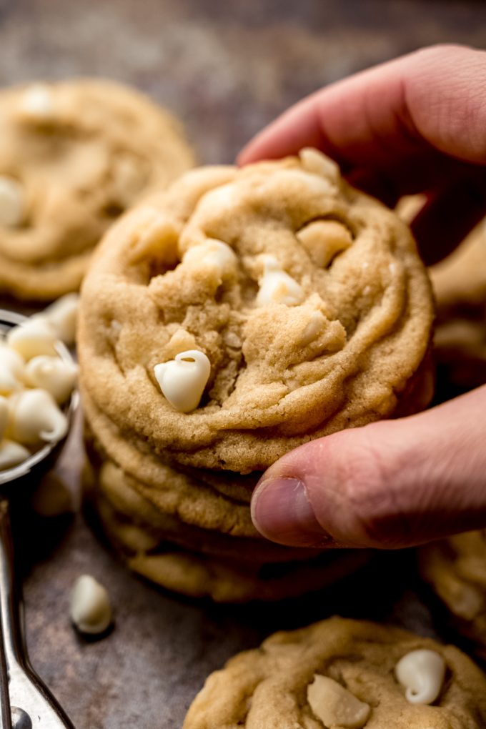 Someone is holding the white chocolate macadamia nut cookie sitting on a stack of others.