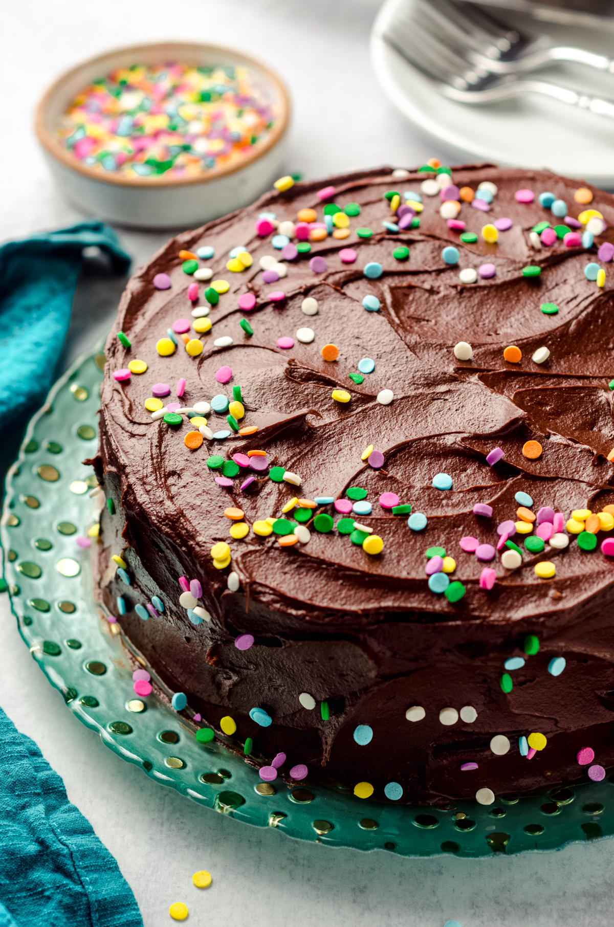 Yellow cake with chocolate frosting and rainbow confetti quins on a plate.