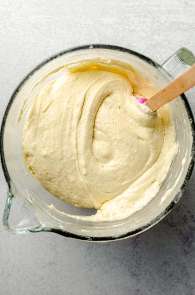 Aerial photo of yellow cake batter in the bowl of a mixer with a spatula.