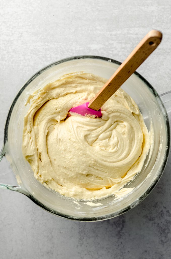 Aerial photo of yellow cake batter in the bowl of a mixer with a spatula.