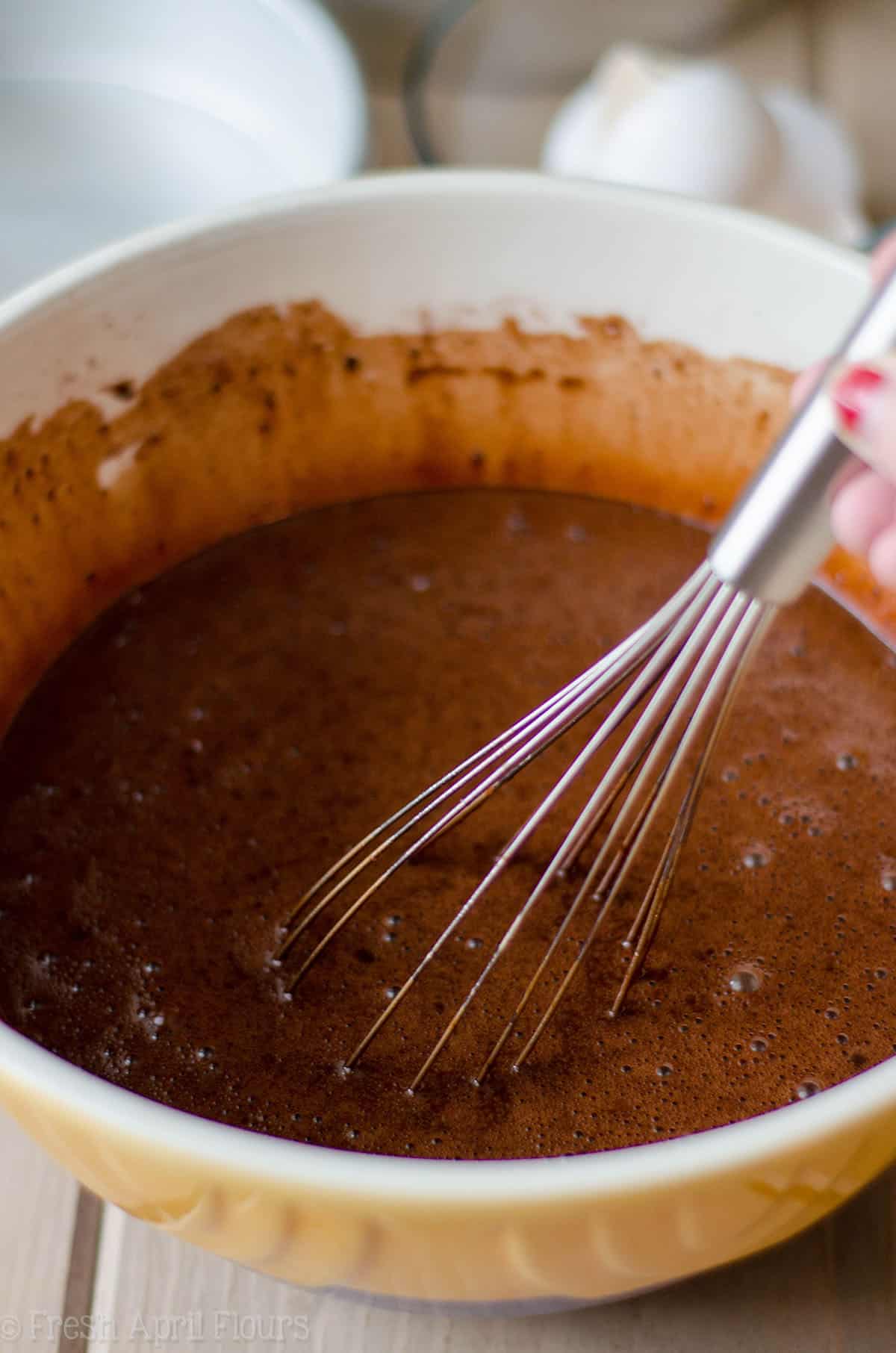 batter for simple chocolate cupcakes in a ceramic bowl getting stirred with a metal whisk