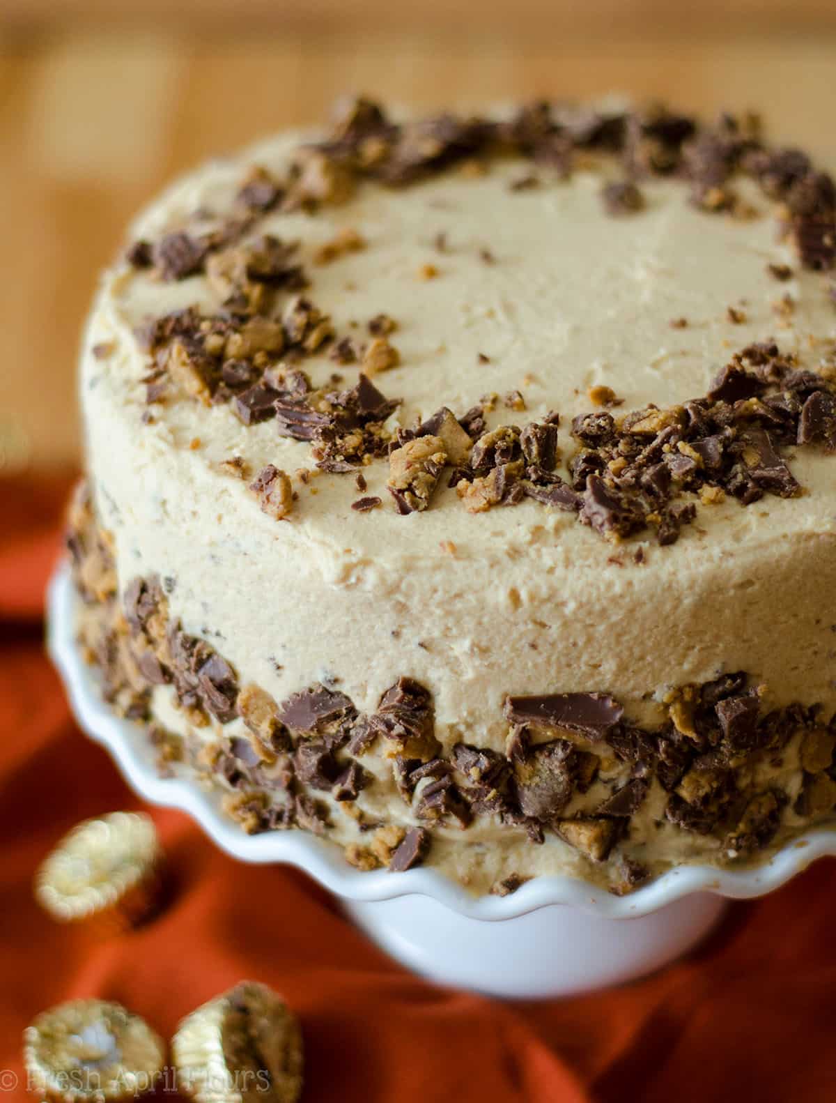 dark chocolate cake with peanut butter frosting and chopped reese's peanut butter cups on it on a cake stand