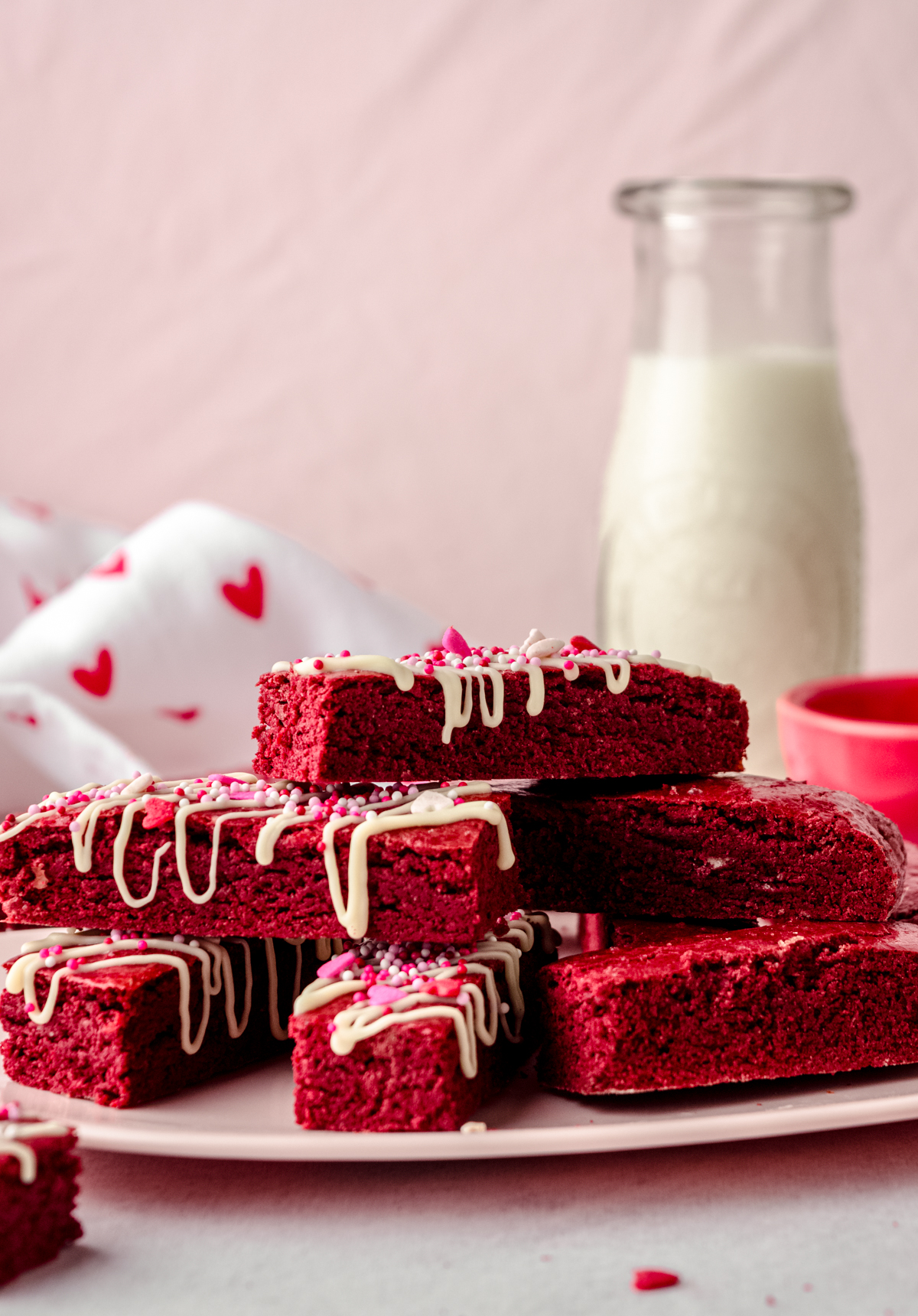 A stack of red velvet biscotti on a plate with milk in the background.