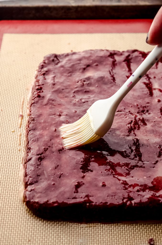 Someone is brushing a red velvet biscotti slab of dough with an egg wash.