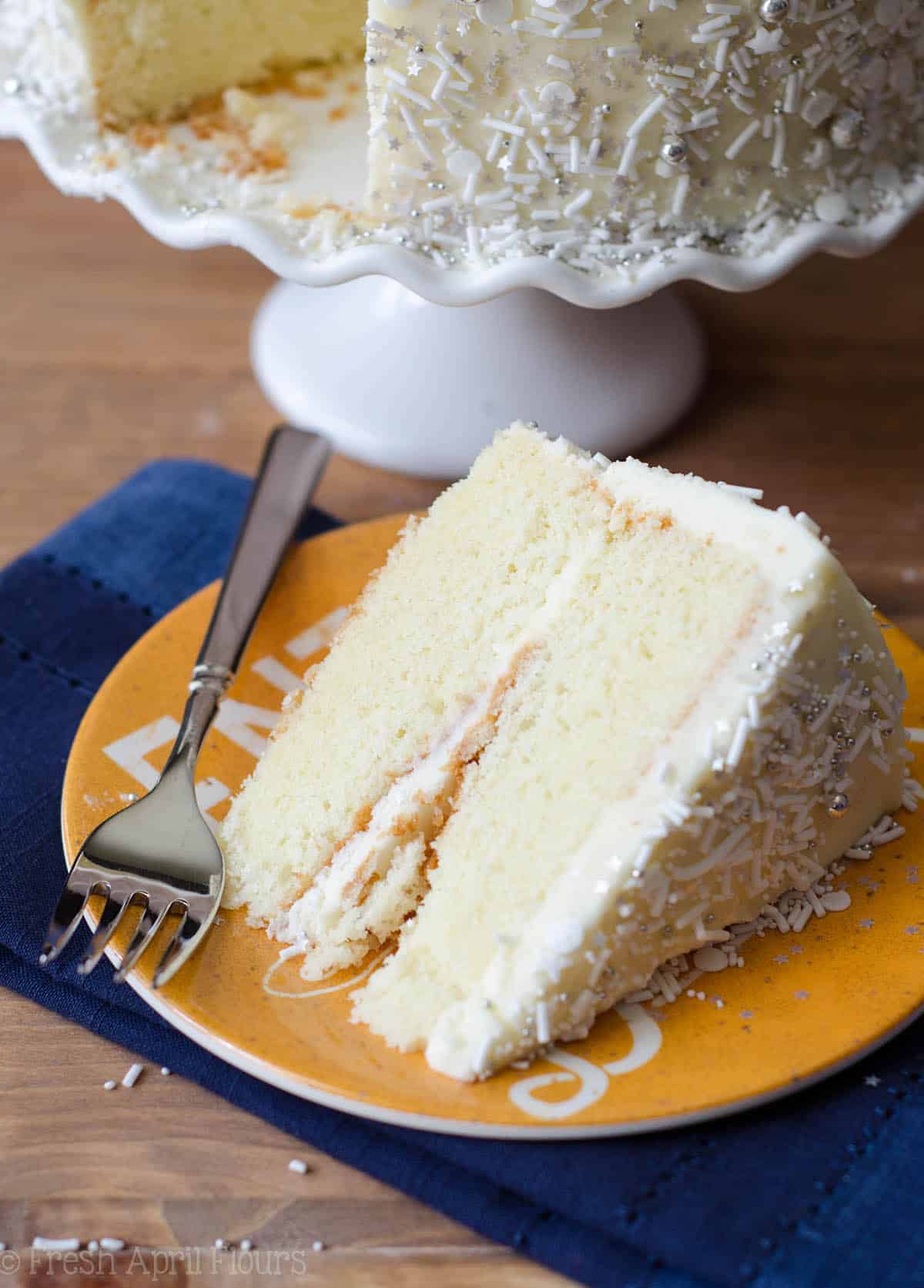 white layer cake with whipped cream buttercream sitting on a yellow plate with a fork
