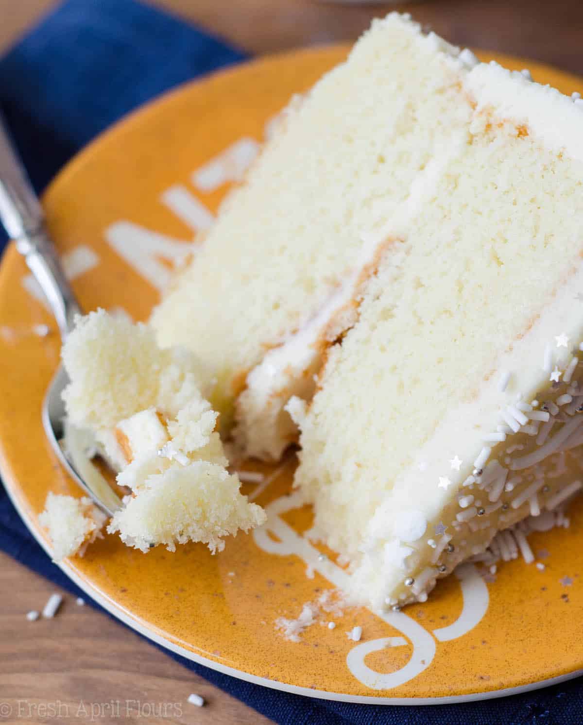 white layer cake with whipped cream buttercream sitting on a yellow plate with a fork full of a bite of cake