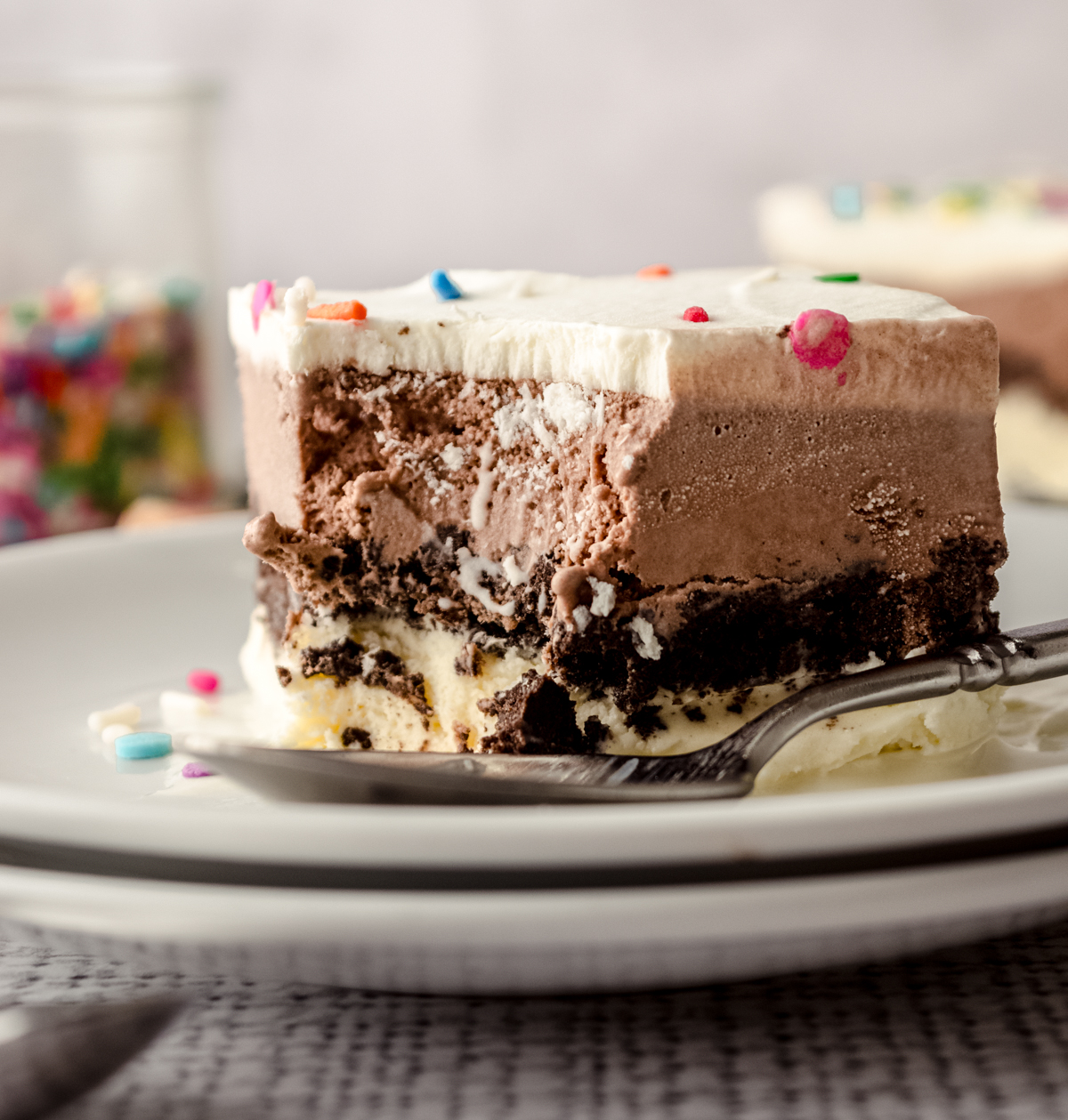 A slice of ice cream sheet cake on a plate with a spoon and a bite taken out of it.