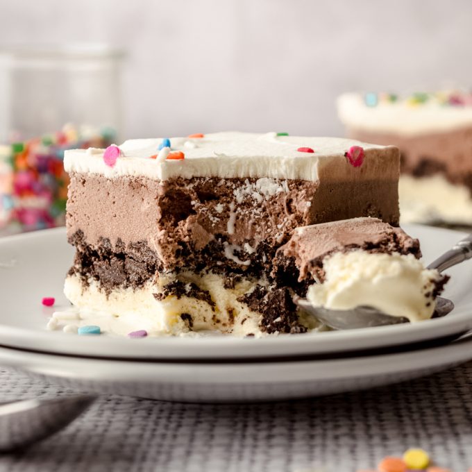 A slice of ice cream sheet cake on a plate with a spoon and a bite taken out of it.