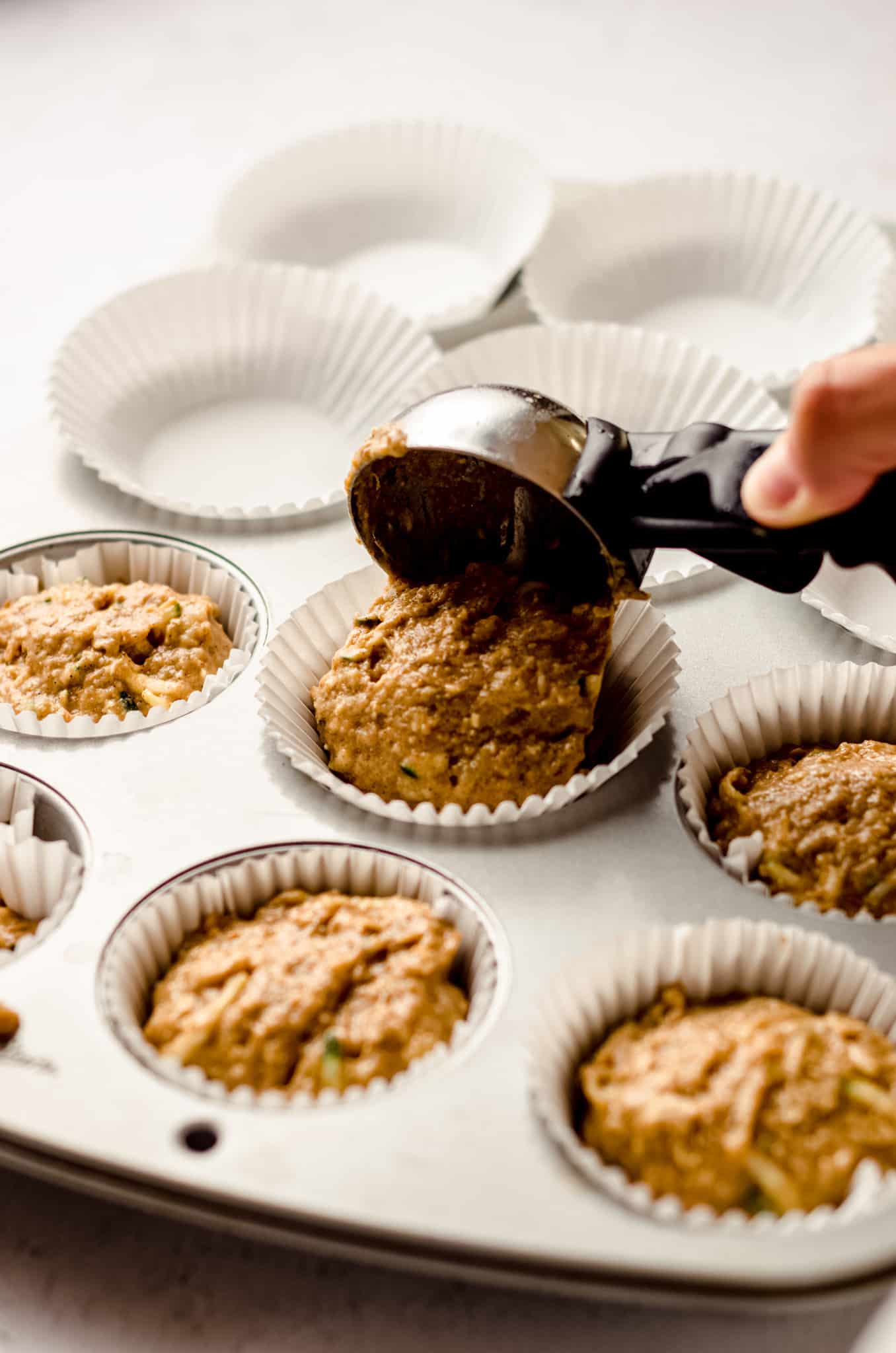 using an ice cream scoop to put muffin batter into a cupcake liner