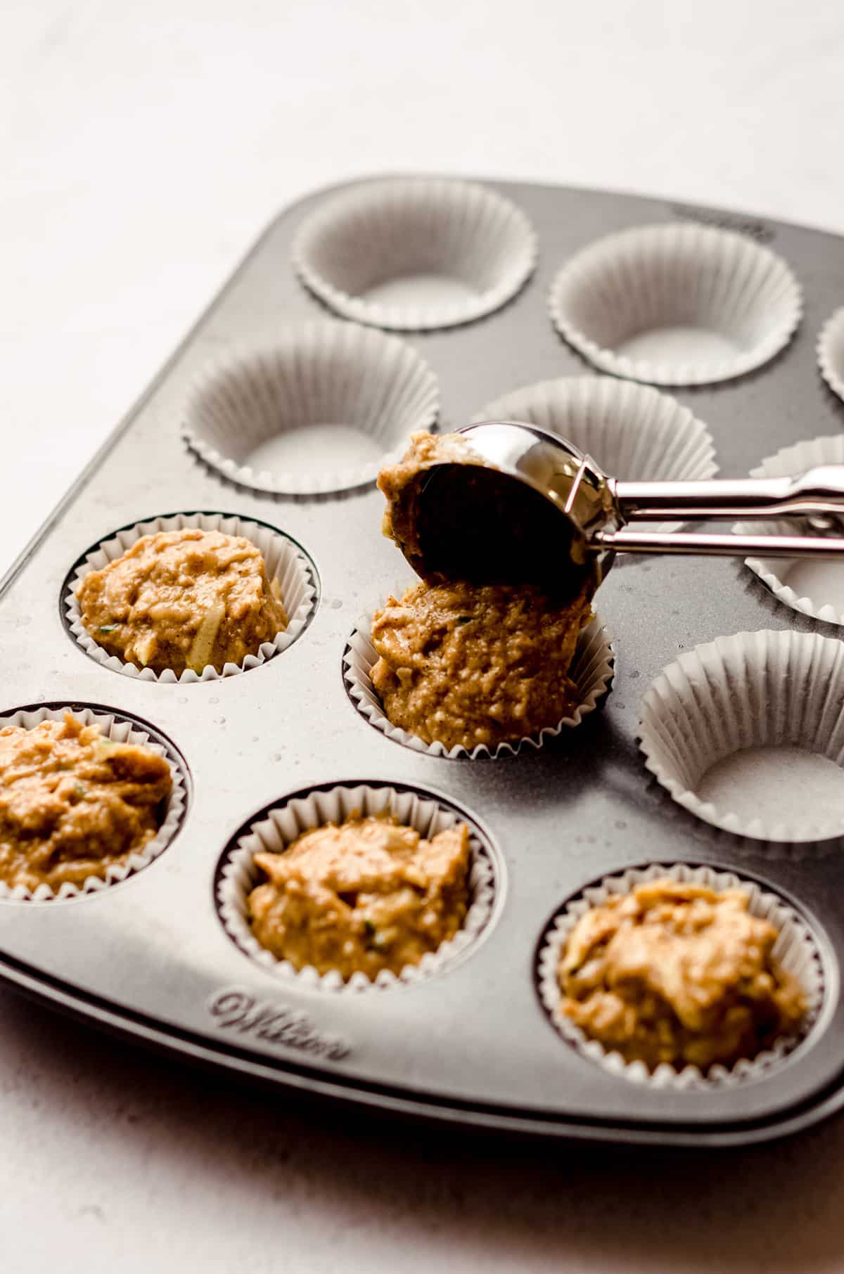 using a cookie scoop to put muffin batter into a mini cupcake liner