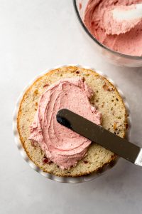 Aerial photo of someone spreading strawberry frosting onto a layer of strawberry cake.