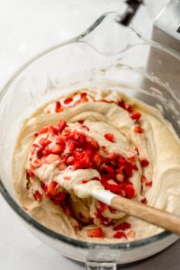 Strawberry cake batter in the bowl of a stand mixer being stirred with a spatula.