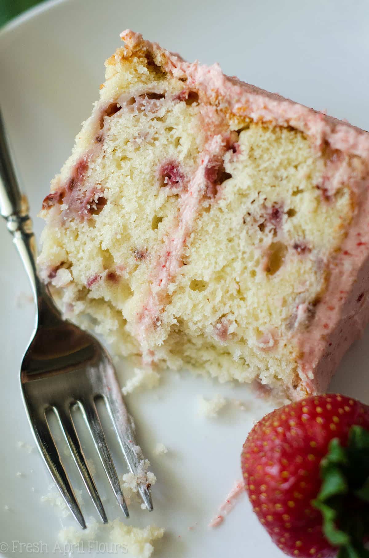 fresh strawberry cake on a plate with a fork and a bite taken out of it