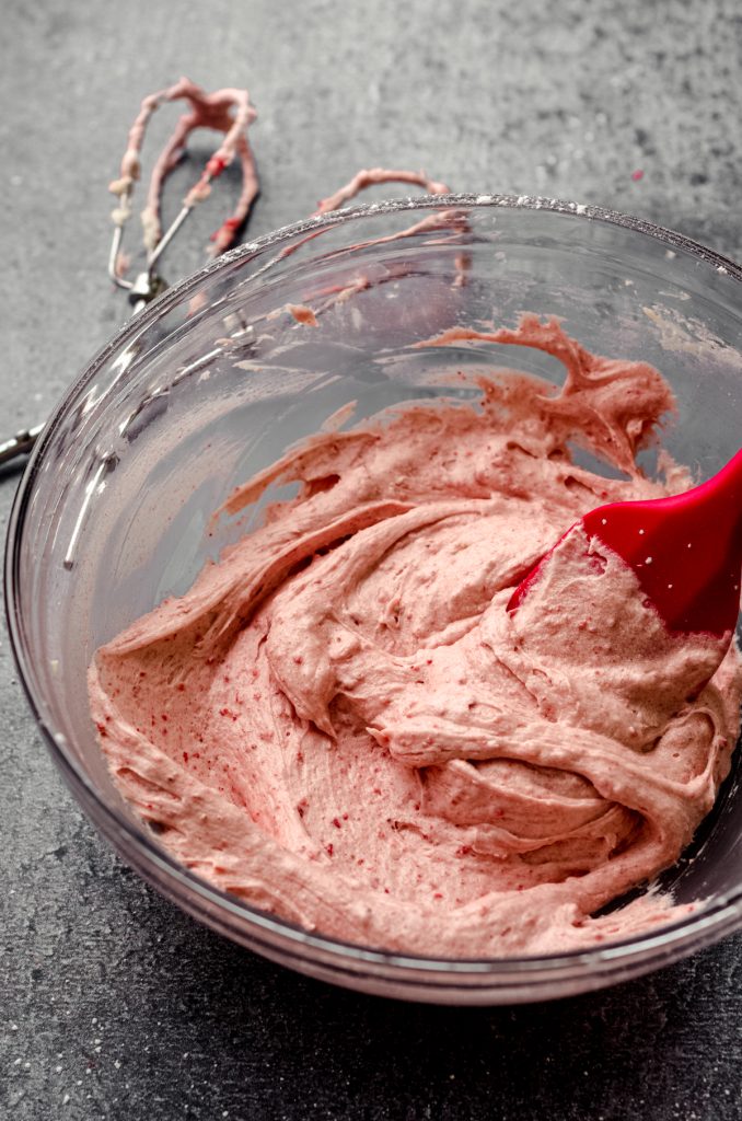 Bowl of strawberry frosting with a spatula in it.