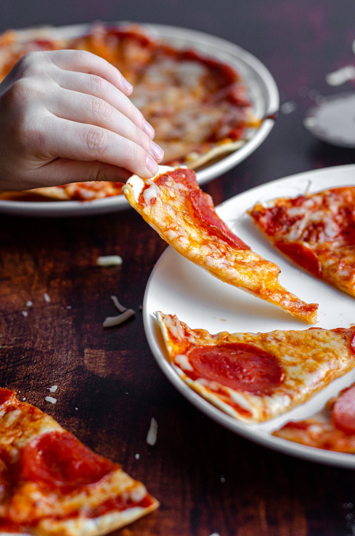 toddler hand grabbing a slice of personal tortilla pizza from a plate