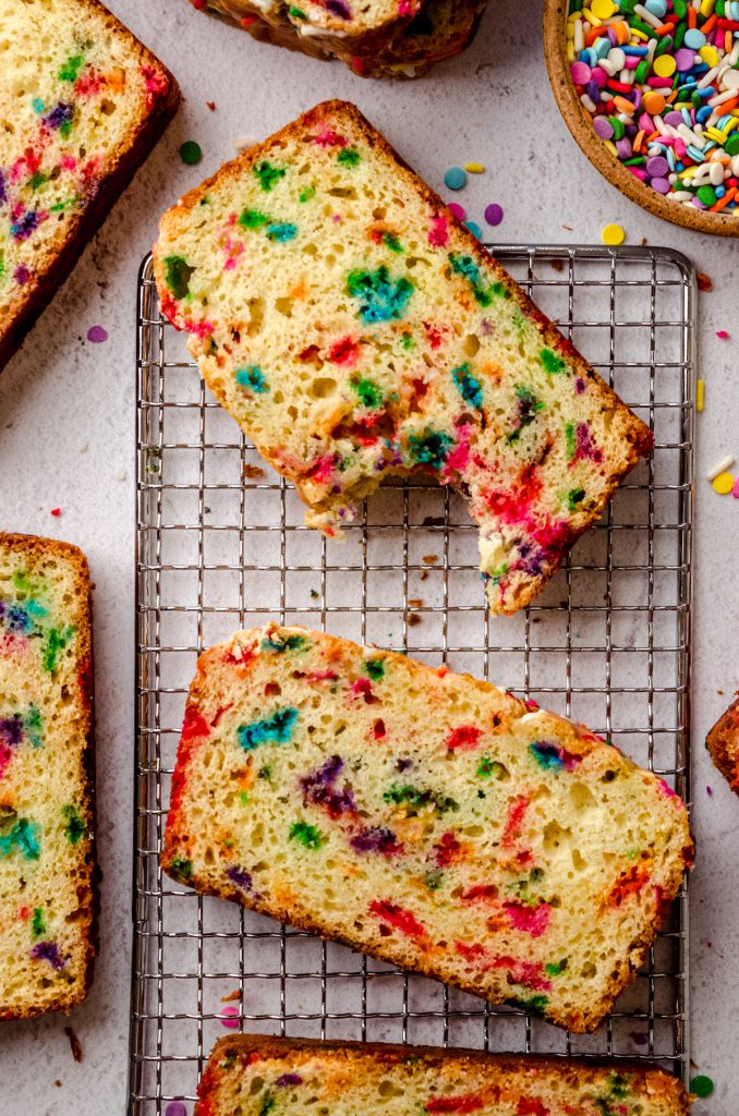 Aerial photo of slices of funfetti bread on a wire cooling rack and one of them has a bite taken out of it.