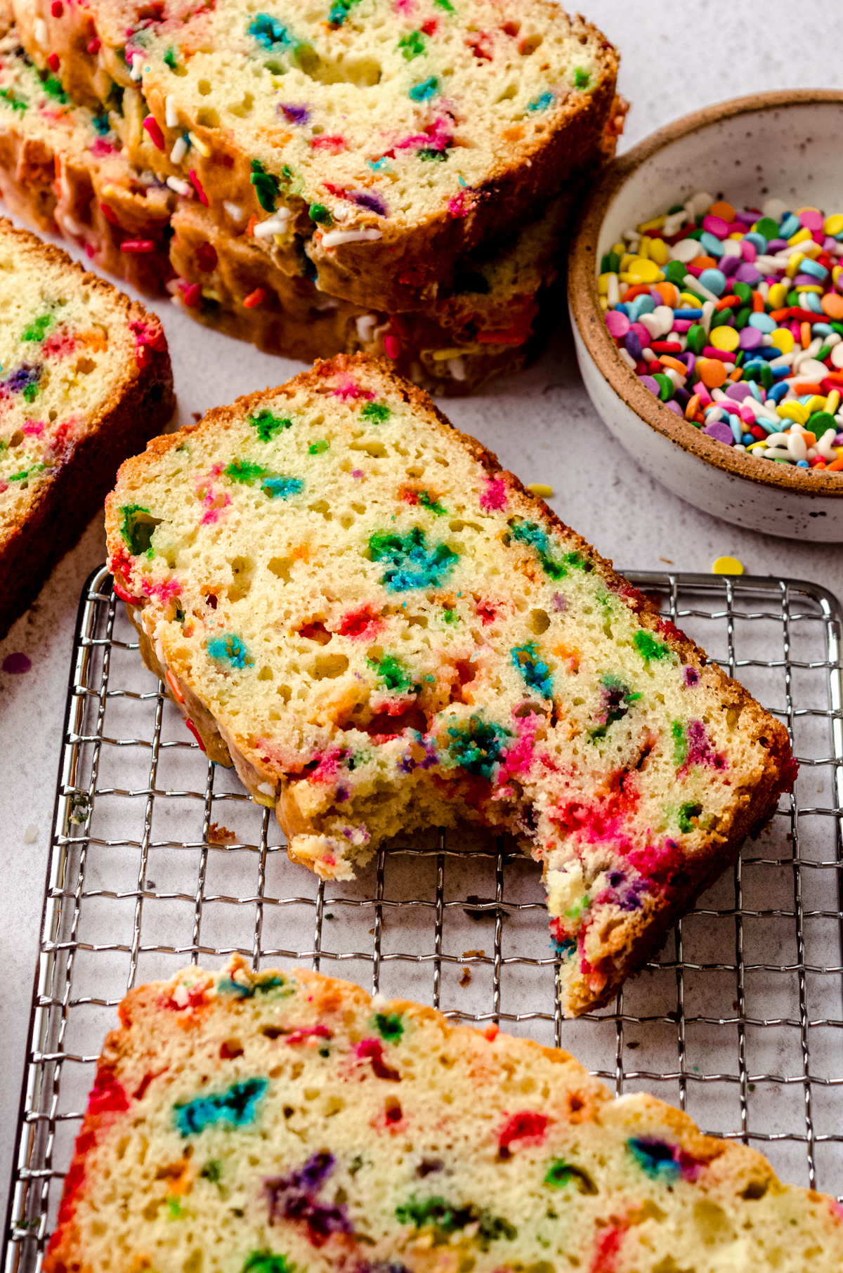Slices of funfetti bread on a wire cooling rack and one of them has a bite taken out of it.