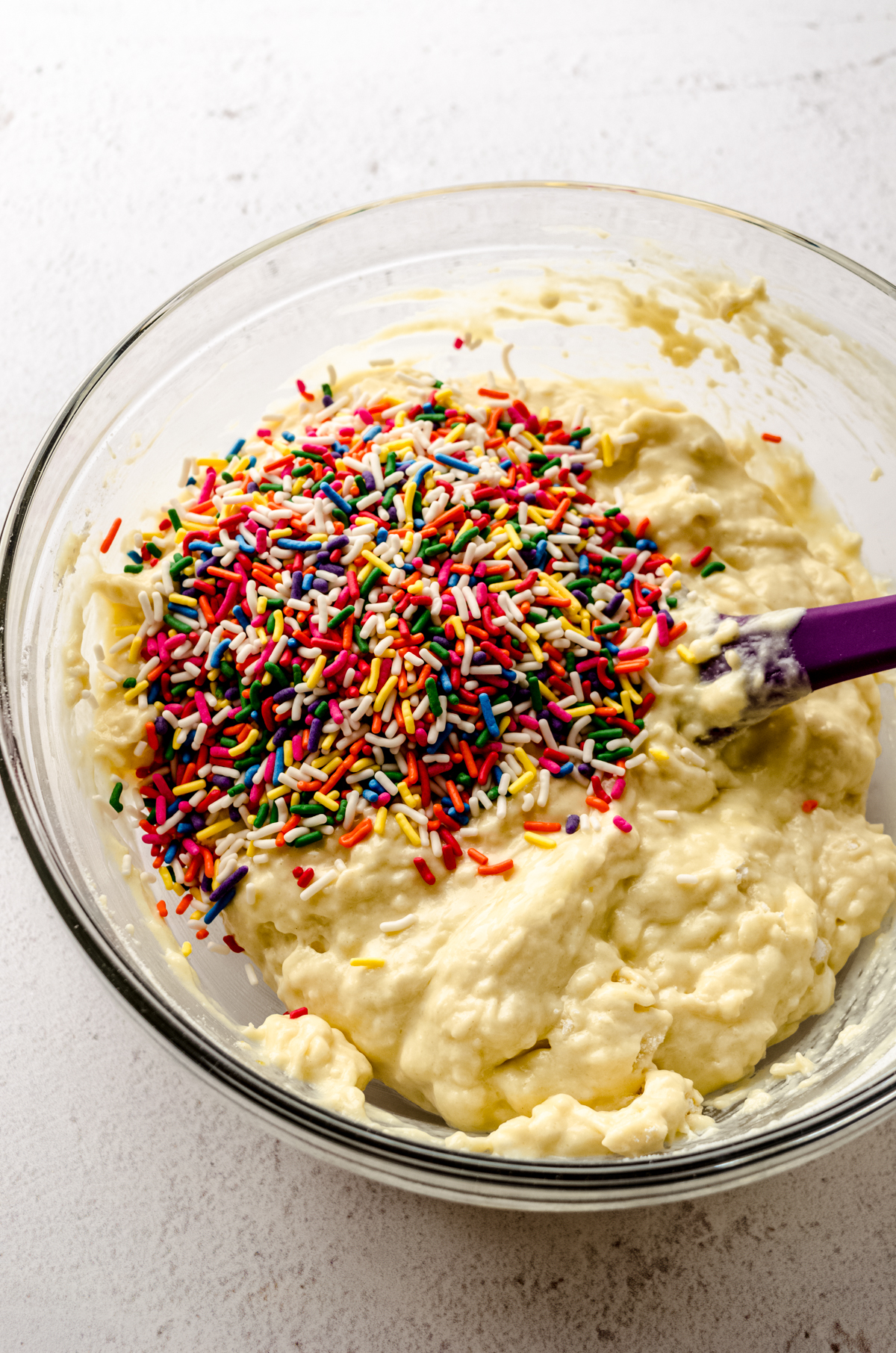 Batter for funfetti bread in a large glass bowl with a spatula.