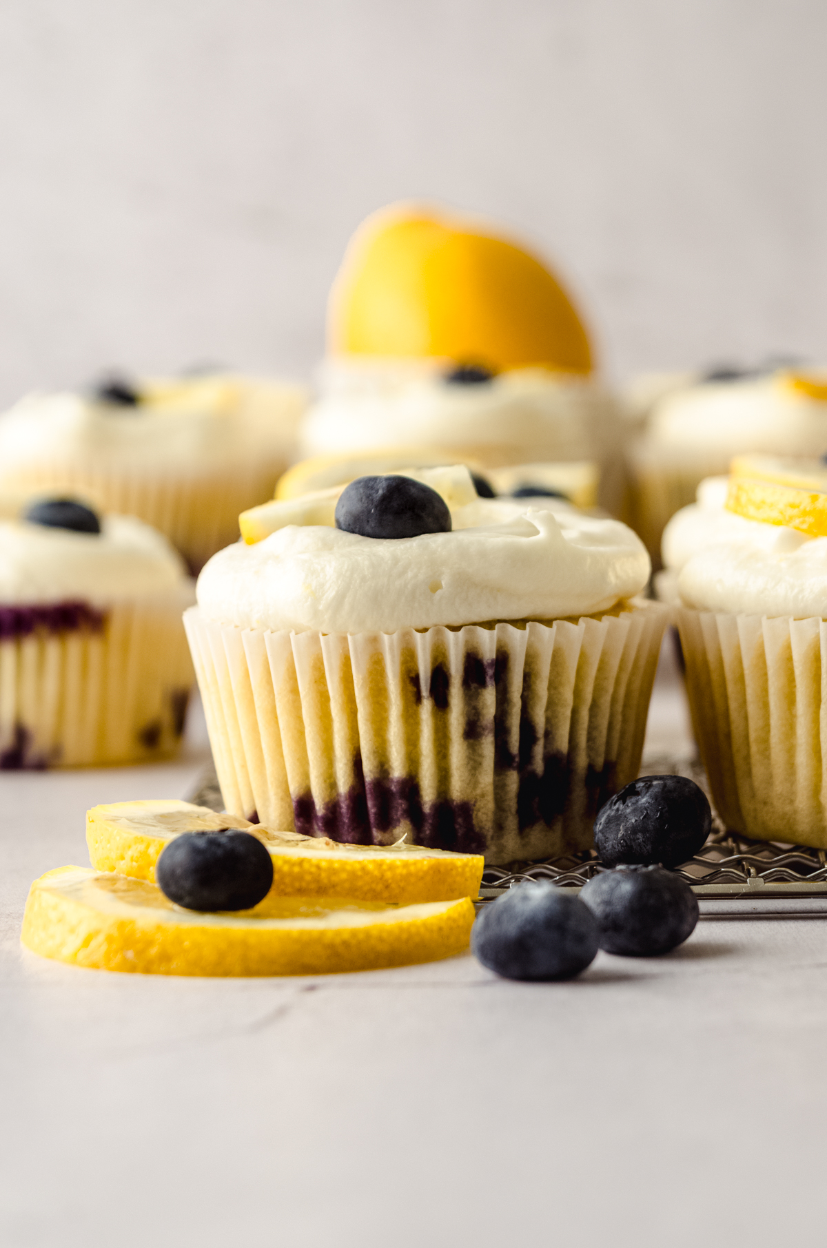 A lemon blueberry cupcake sitting on a metal grater with a blueberry on top and a lemon slice on top and beside it.