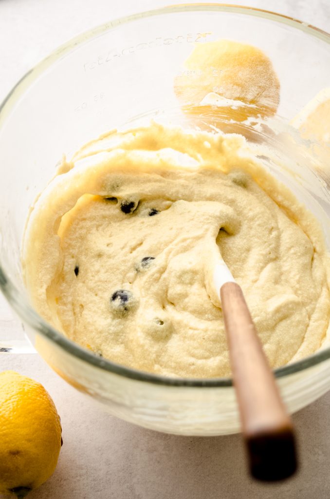 Lemon blueberry cupcake batter in a large bowl with a spatula in it.