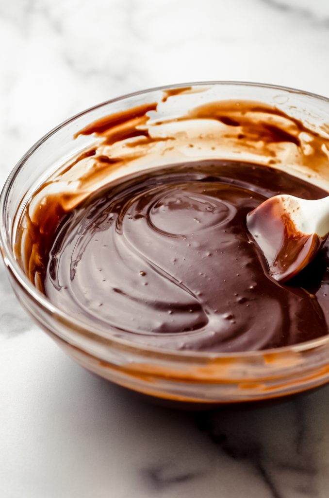 Chocolate ganache in a glass bowl with a spatula.