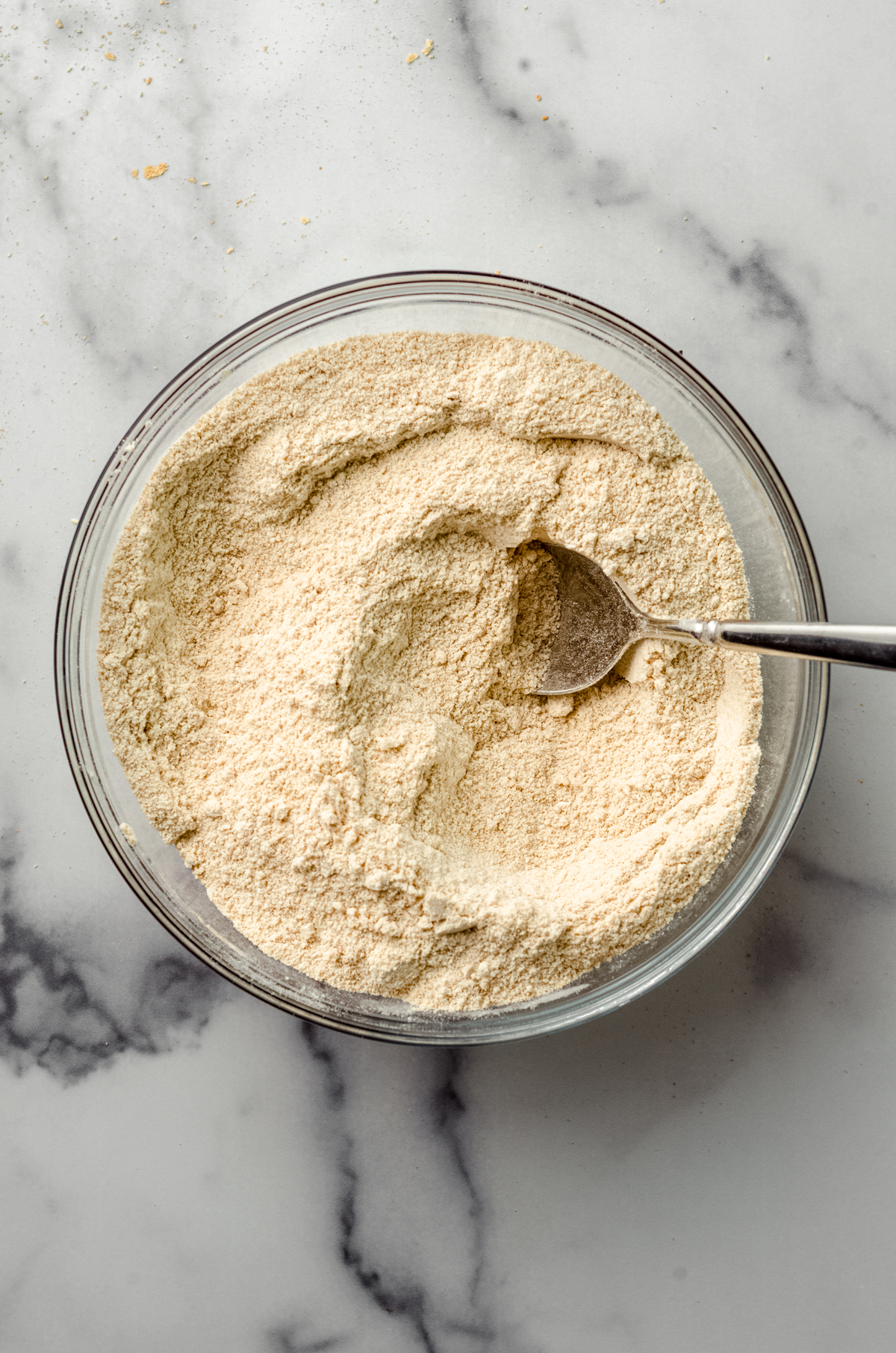 Dry ingredients for graham cracker cookies in a glass bowl with a spoon.