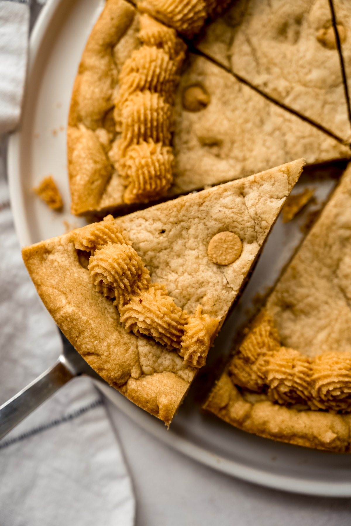 Aerial photo of someone removing a slice of peanut butter cookie cake with a server.