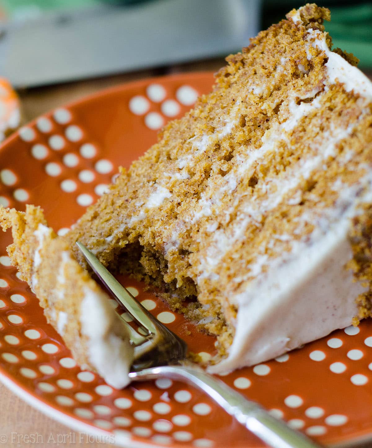 brown butter pumpkin cake with maple cinnamon cream cheese frosting on an orange and white polka dot plate with a fork