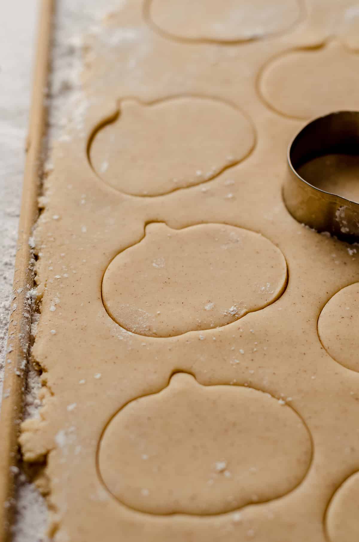 pumpkin spice sugar cookie dough being cut out with a pumpkin cookie cutter