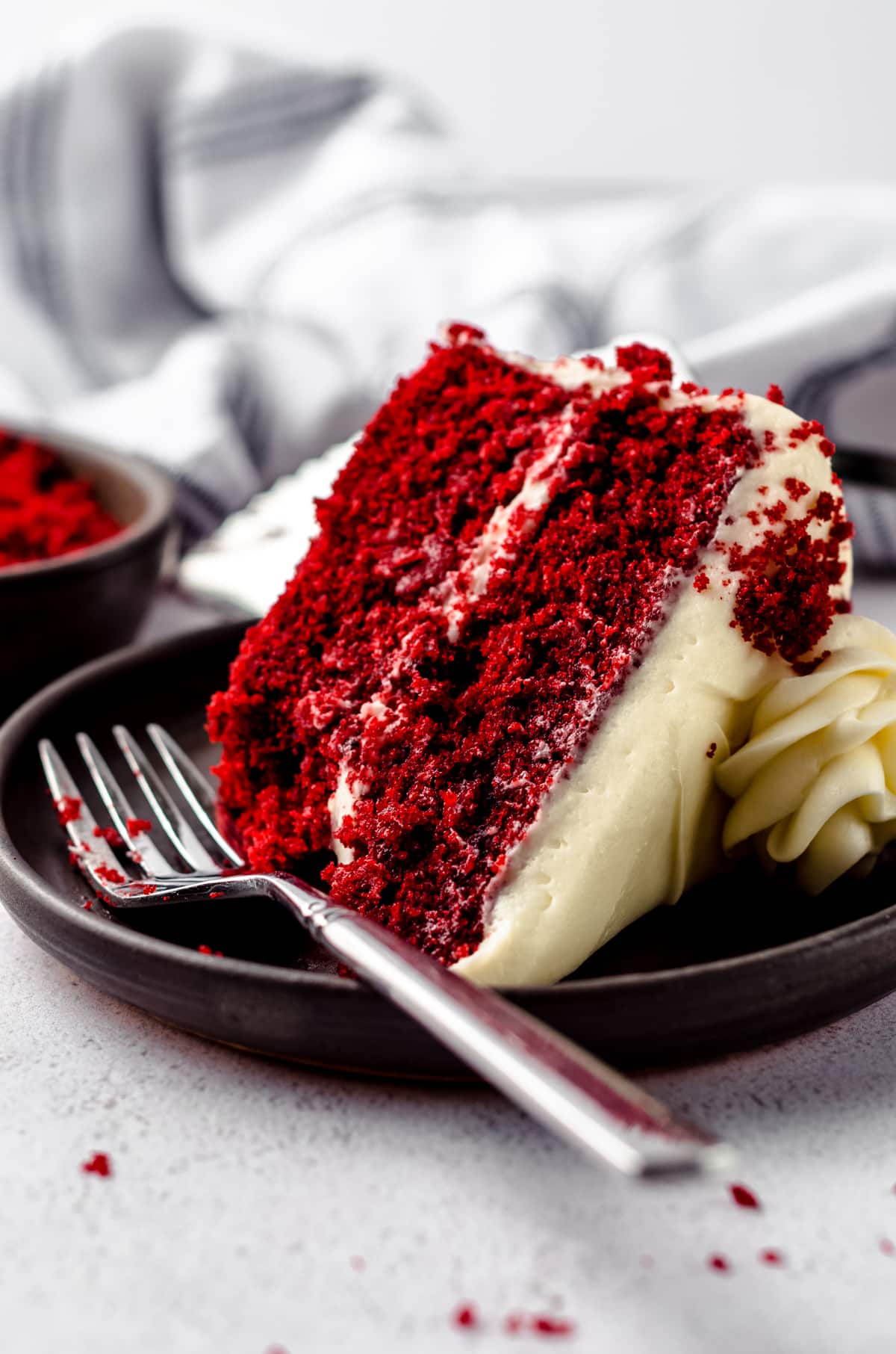 A slice of red velvet cake on a plate with a fork and a bite taken out of it.