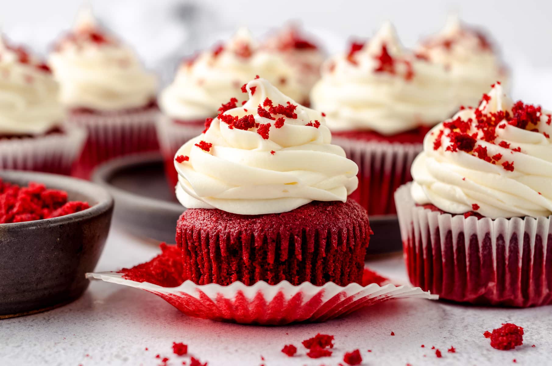 Red velvet cupcakes with cream cheese frosting and red velvet crumbs on top. The one in the front has the wrapper pulled down.