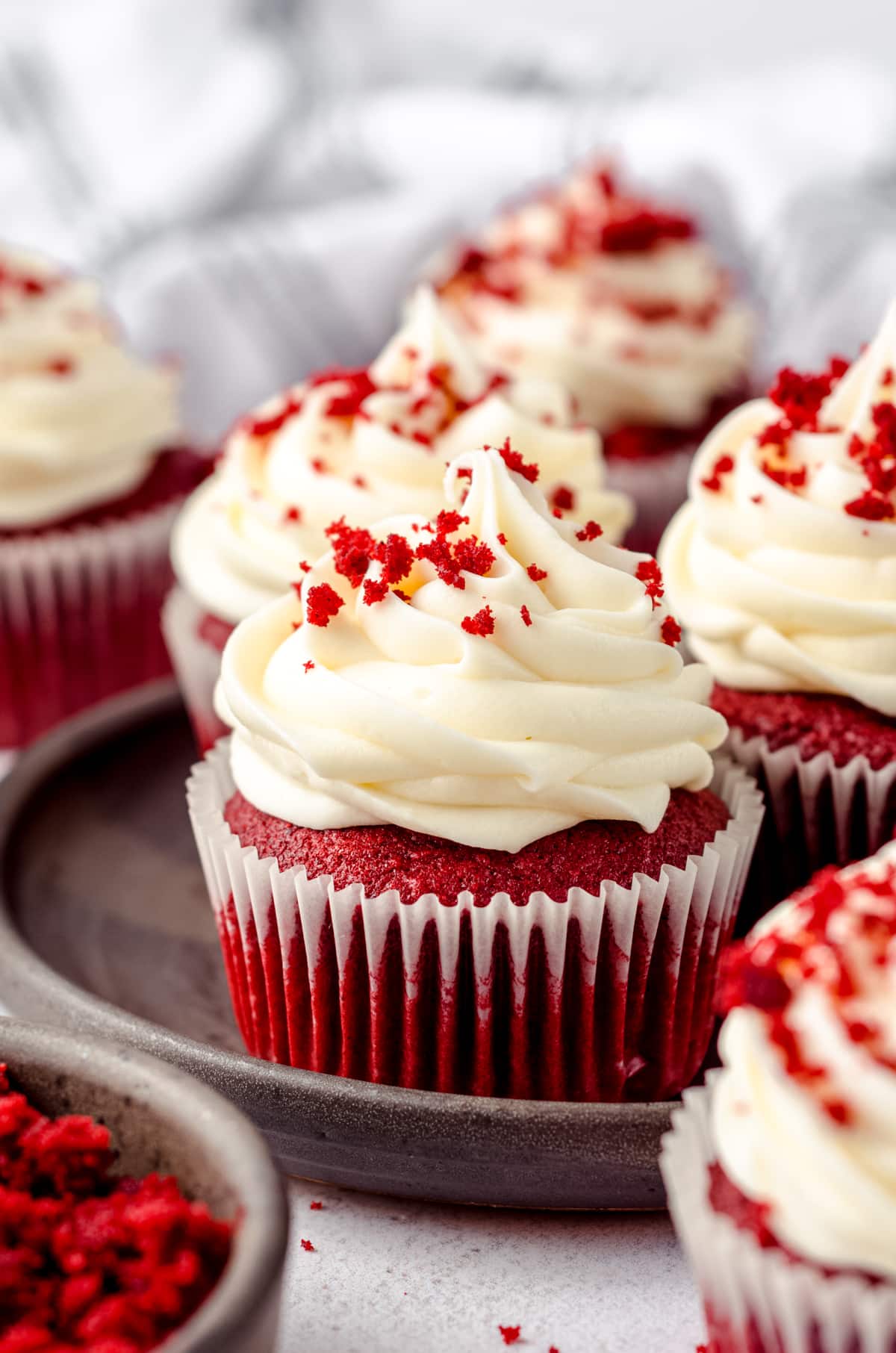 A plate of red velvet cupcakes with cream cheese frosting and red velvet crumbs on top.