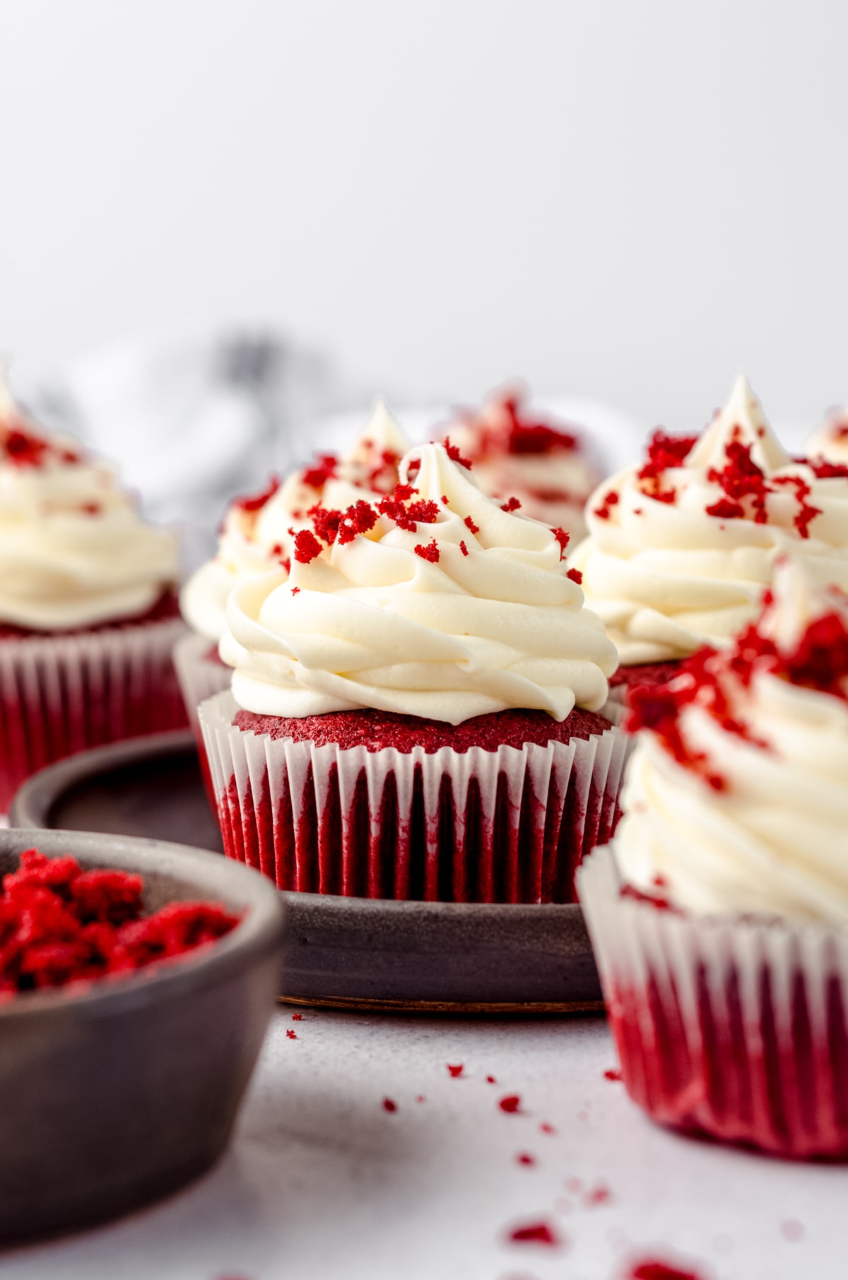 A plate of red velvet cupcakes with cream cheese frosting and red velvet crumbs on top.