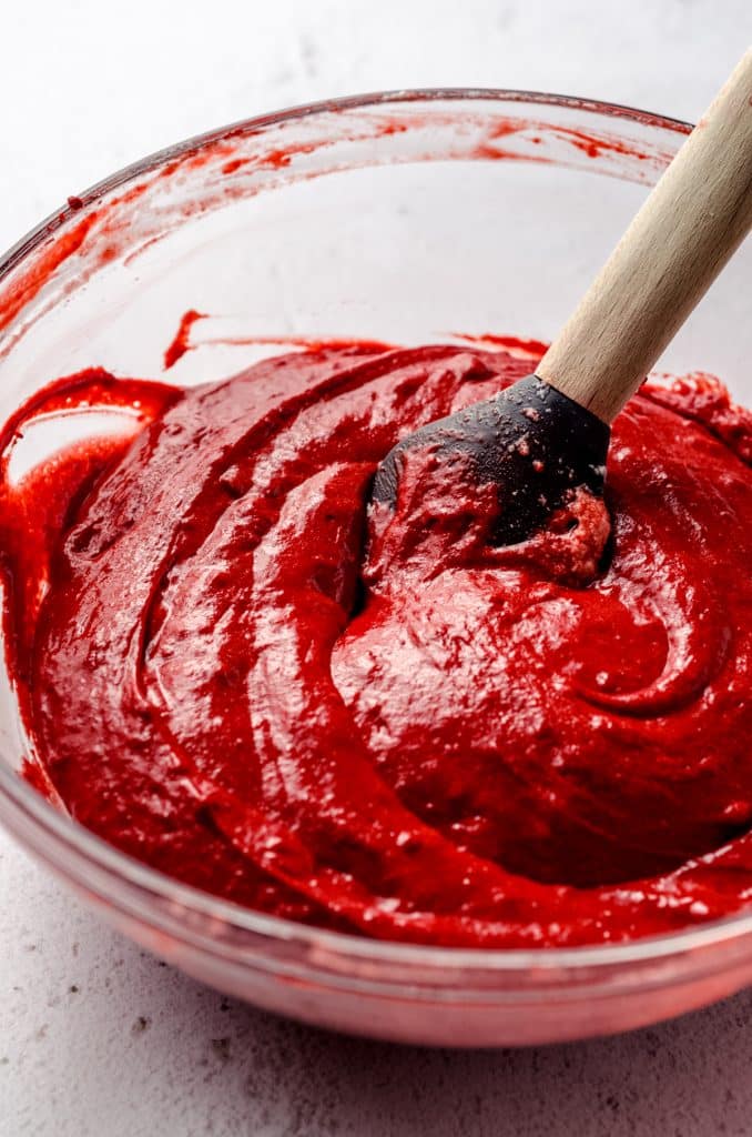 Smooth red velvet cupcake batter in a glass bowl with a spatula.
