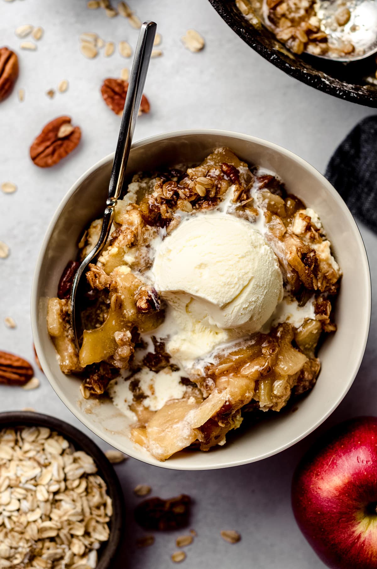 aerial photo of warm apple crisp in a bowl with a scoop of melting vanilla ice cream