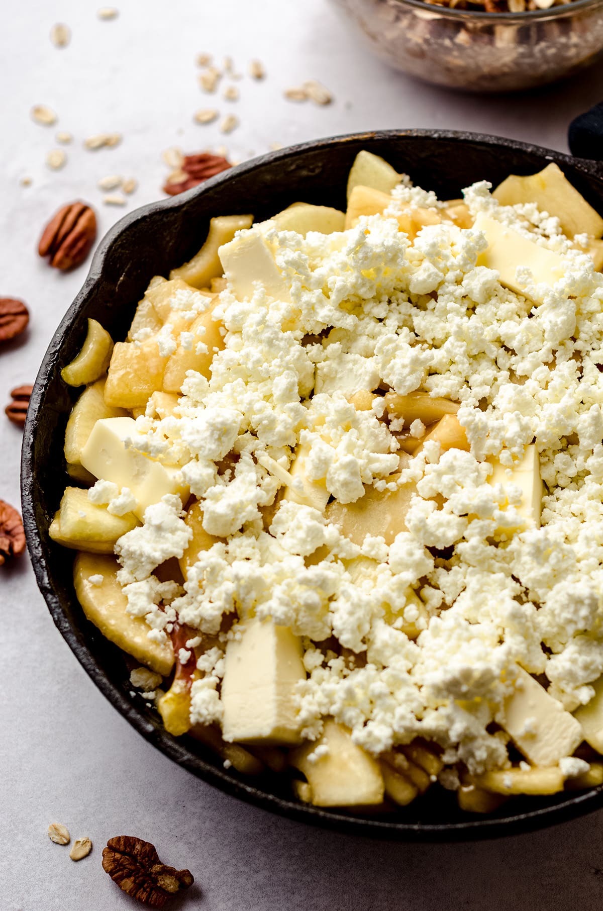 apples in a skillet covered with crumbled goat cheese for apple crisp