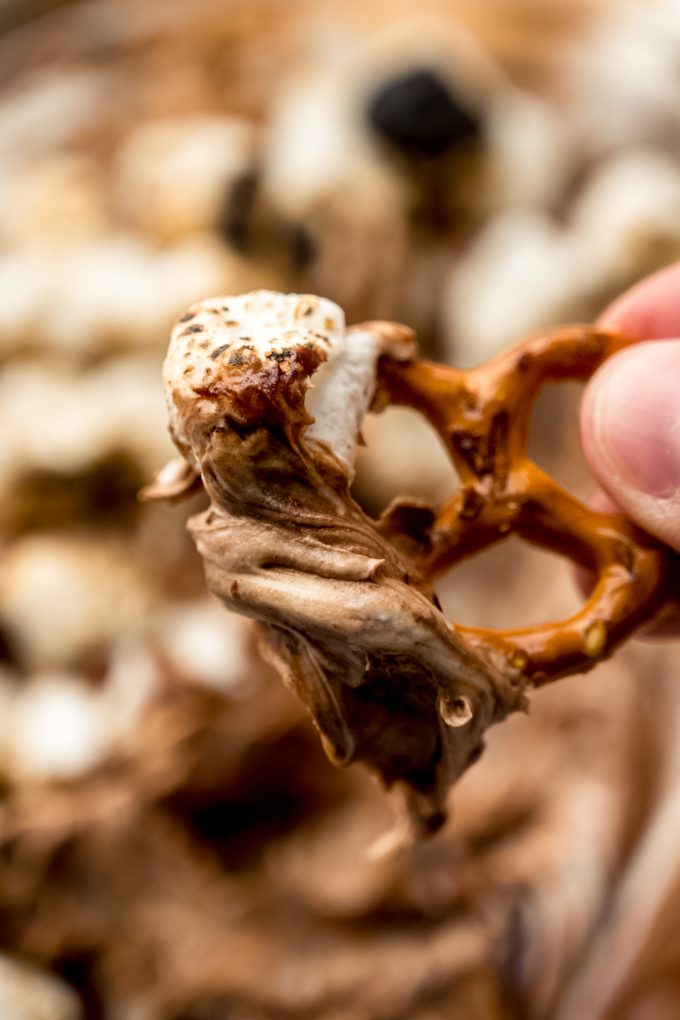 Someone is holding a mini pretzel that has been dipped into s'mores dip.