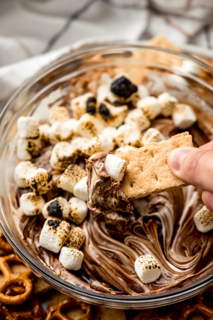 Someone is dipping a graham cracker into s'mores dip.