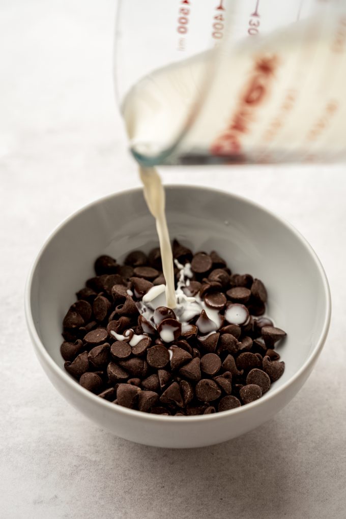 Someone is pouring hot cream onto a bowl of chocolate to make chocolate ganache.