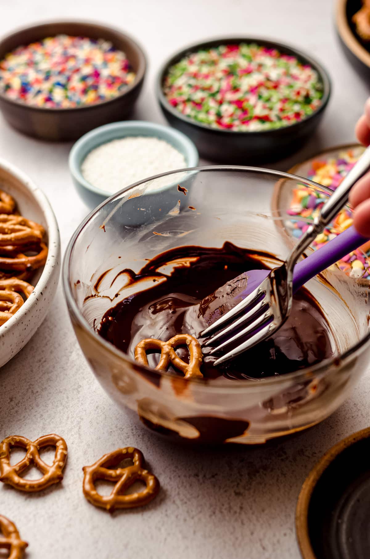 using a fork to dip mini pretzels in melted chocolate