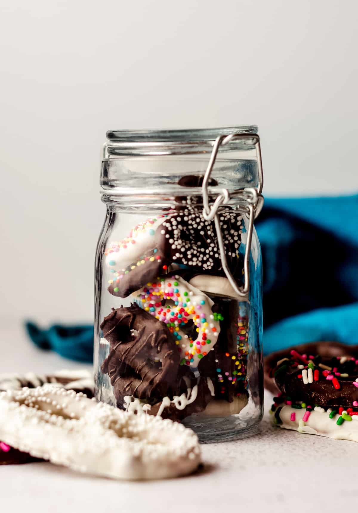 chocolate covered pretzels decorated with assorted sprinkles in a glass jar