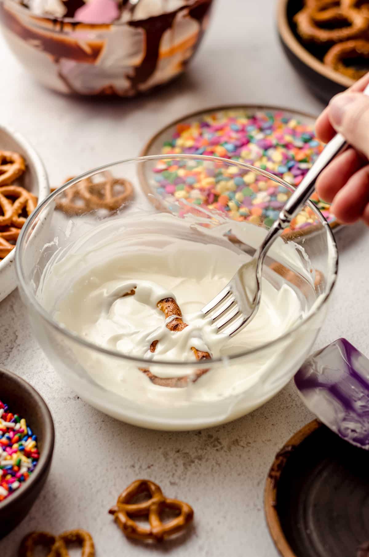 using a fork to dip pretzels in melted white chocolate