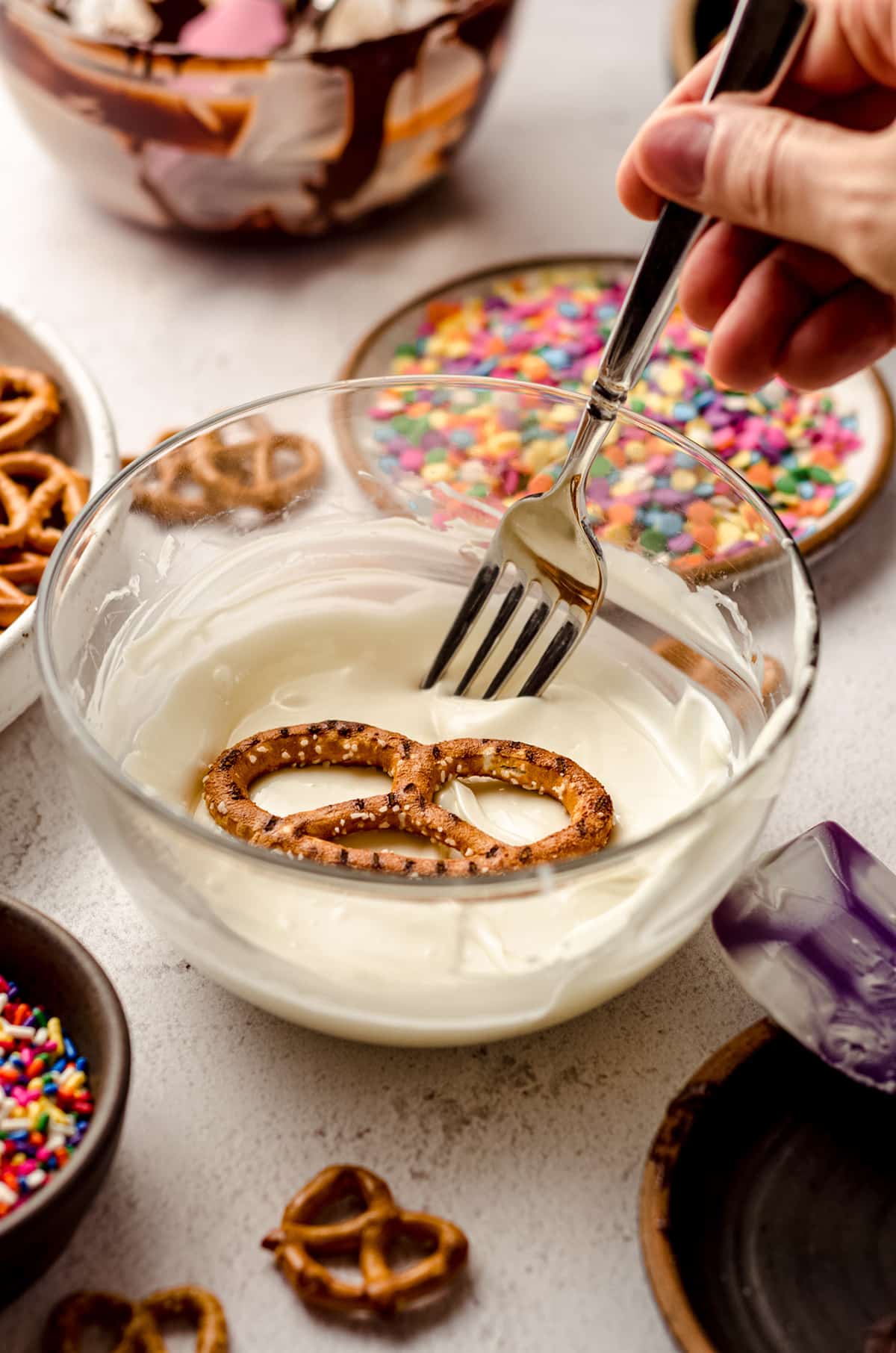 using a fork to dip pretzels in melted white chocolate