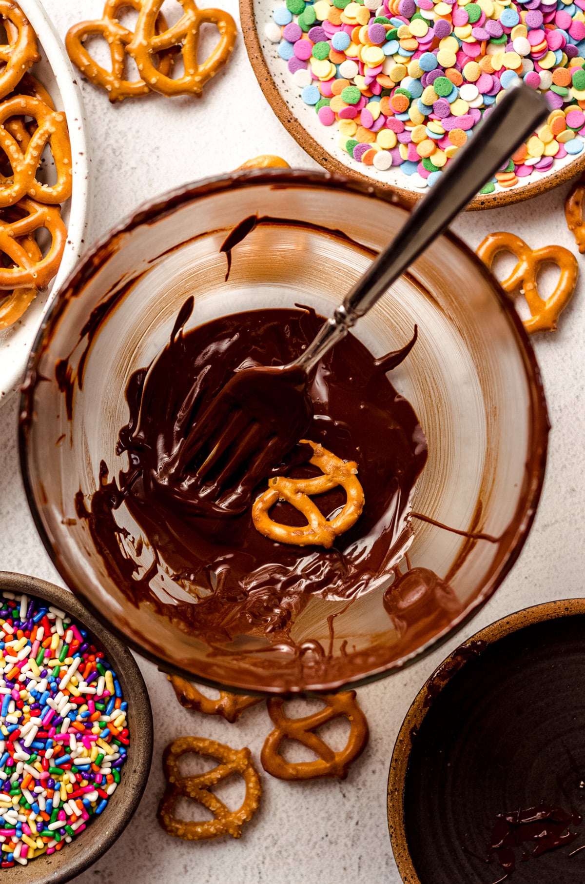 using a fork to dip mini pretzels in melted chocolate