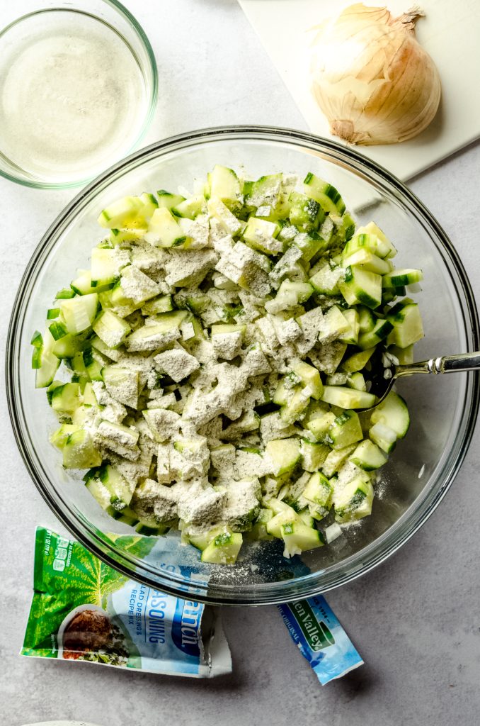 Aerial photo of chopped cucumbers in a bowl with a packet of ranch dressing sprinkled on top.