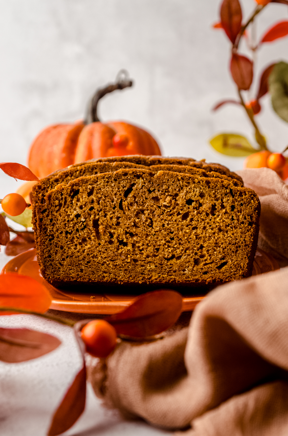 Slices of pumpkin bread loaf on a plate with pumpkins and fall decor in the background.