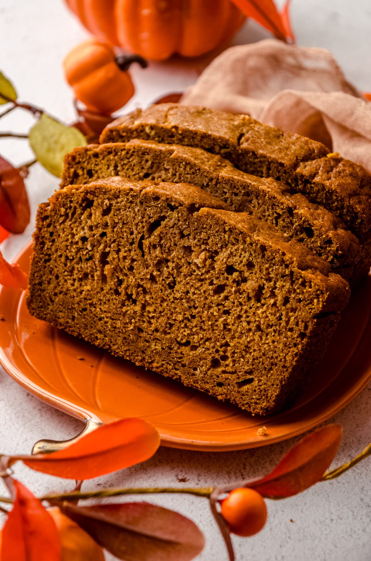 Slices of pumpkin bread loaf on a plate with pumpkins and fall decor in the background.