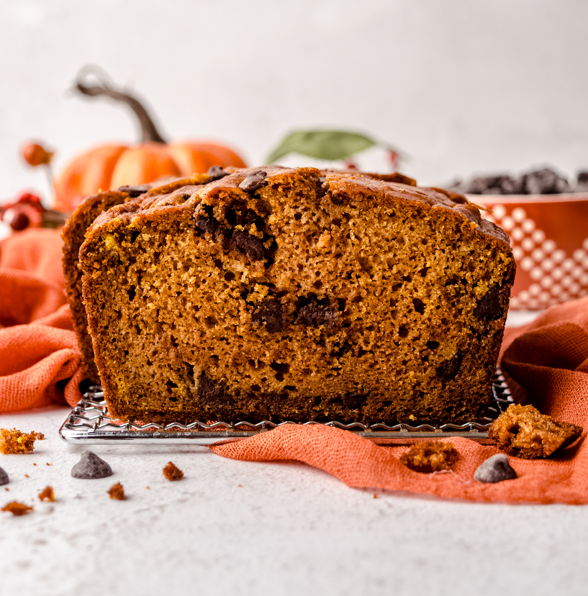 Chocolate chip pumpkin bread slices on a wire cooling rack with pumpkins and fall decor in the background.